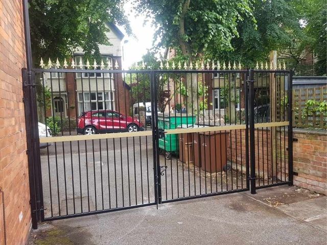 Black metal driveway gates topped with gold fleur de lis, fitted between brick walls