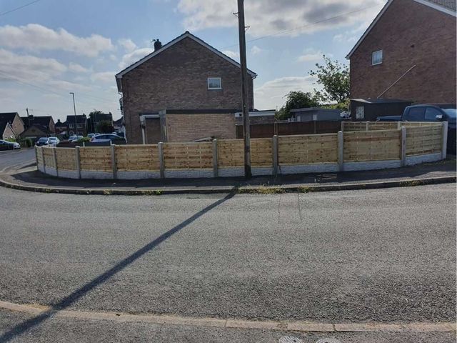 Hit and miss fencing following a curved corner plot boundary in concrete posts with rock faced gravel boards