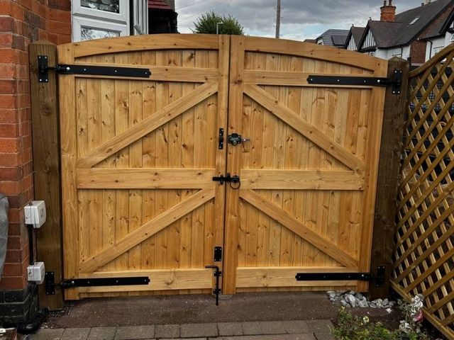 The same arched wooden driveway gates from inside the drive showing the braced frame, black tee hinges and slide bolts