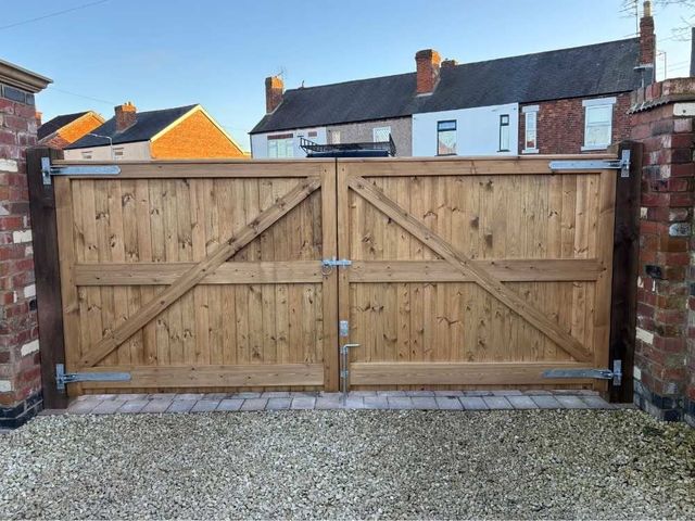 The same wide wooden driveway gates from inside showing galvanised strap hinges, braced frame and a drop bolt into the gravel