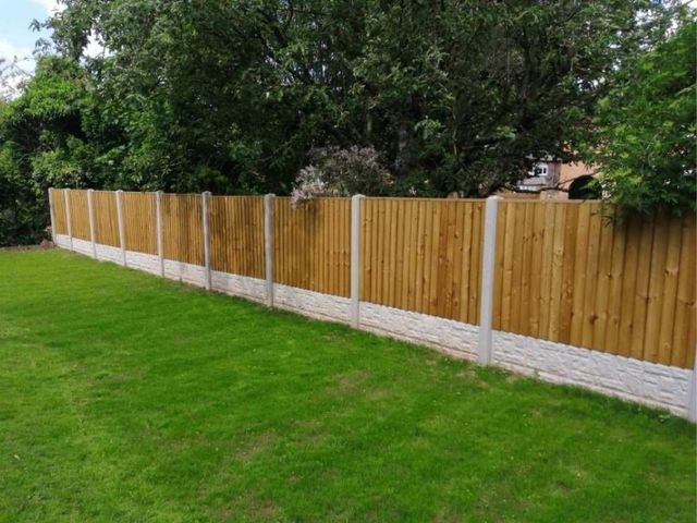 Long straight run of closeboard fence panels in new concrete posts with rock faced gravel boards along a lawn