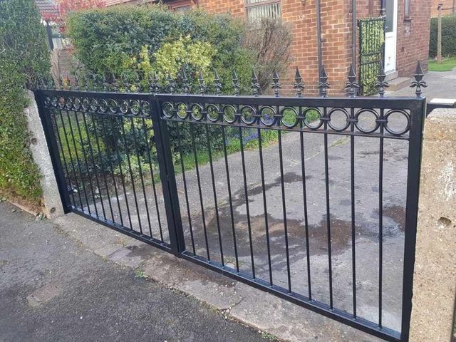 Black metal driveway gates with a band of ring detailing below fleur de lis finials