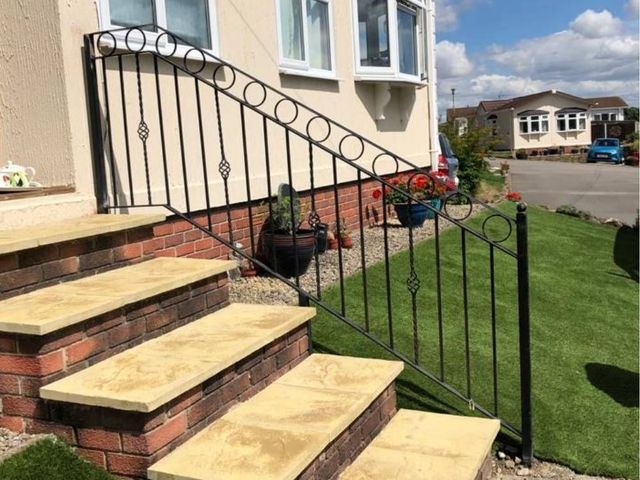 Decorative metal handrail with rings and twisted bar alongside sandstone steps to a front door