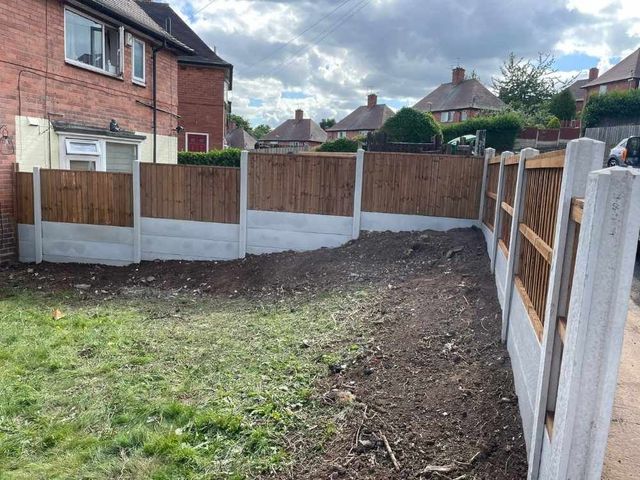 Closeboard fence panels in concrete posts with gravel boards holding back banked soil on a sloping garden boundary mid installation