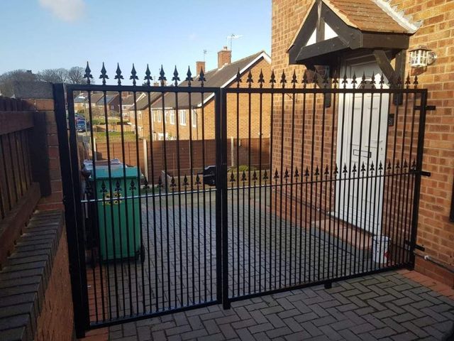 Black metal driveway gates with unequal leaves fitted to an offset opening