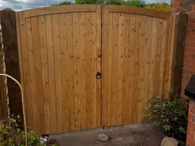 Arched top wooden driveway gates seen from the road side with a smooth boarded face, ring handle and lock