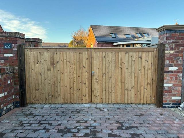 Wide flat topped wooden driveway gates hung between brick piers across a block paved entrance