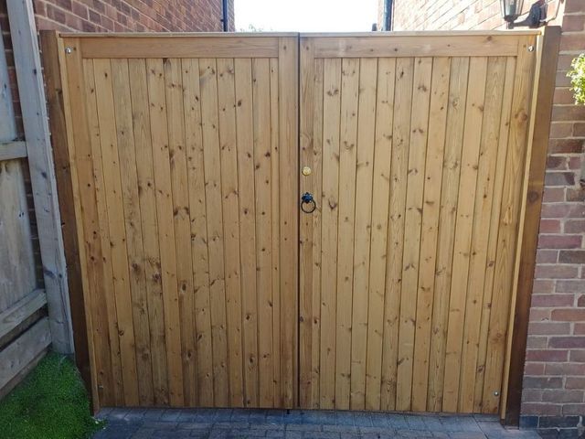 Tongue and groove wooden double gates with a flat top, ring handle and lock, hung between a brick pier and a fence post