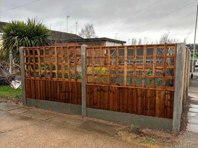 Brown treated board and trellis fence panels in concrete slotted posts with gravel boards beside a pavement