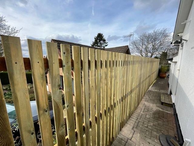 Tall picket fencing running along a narrow block paved side passage beside a rendered house