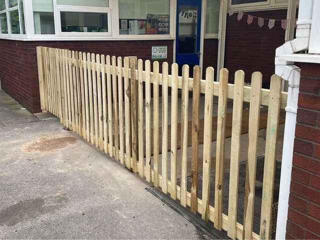 Round top picket fencing fitted on hard standing outside a school entrance with a brick wall behind