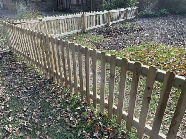 Round top picket fencing enclosing a section of grassed land with a braced gate and a second run behind
