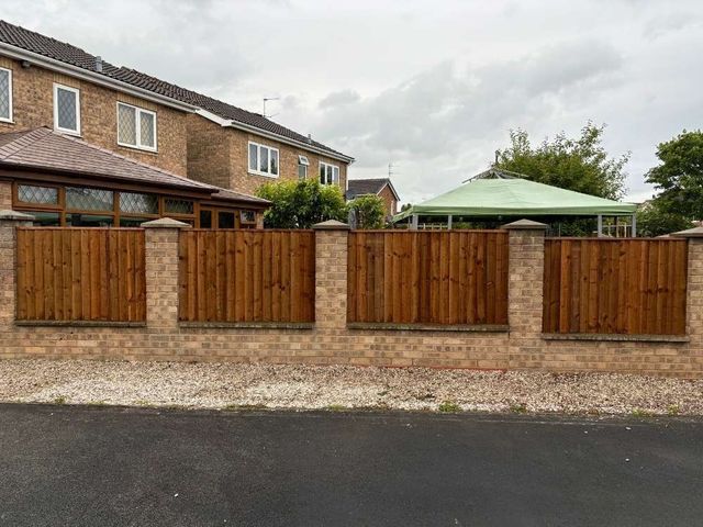 Timber fence panels fitted between brick pillars on top of a low brick wall