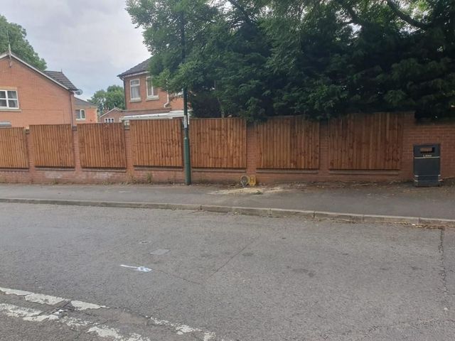 Closeboard timber fencing raising the height of a red brick boundary wall alongside a road