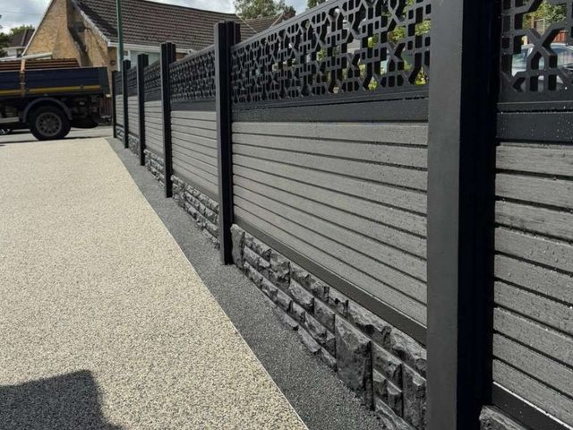 Completed run of grey composite fencing with decorative toppers in black concrete posts and rock-faced gravel boards