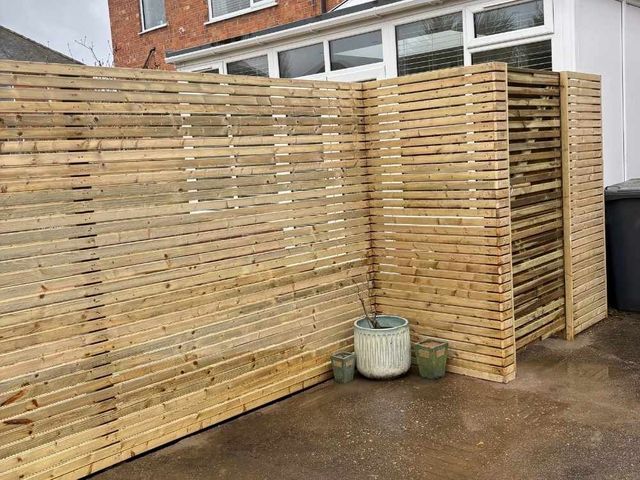Tall slatted fencing returning around a corner beside a conservatory with a matching slatted gate