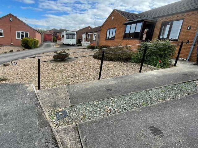 Black metal handrail with a curled end running across a gravelled front garden of a bungalow