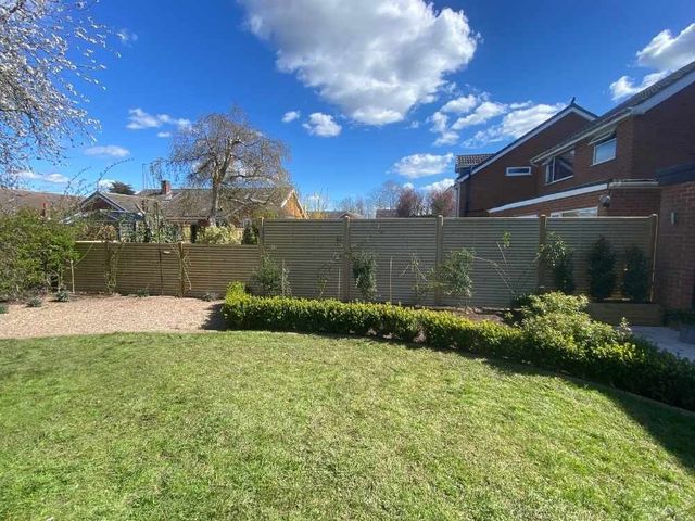 Slatted fence panels stepping down a sloping boundary line in level bays beside newly planted borders