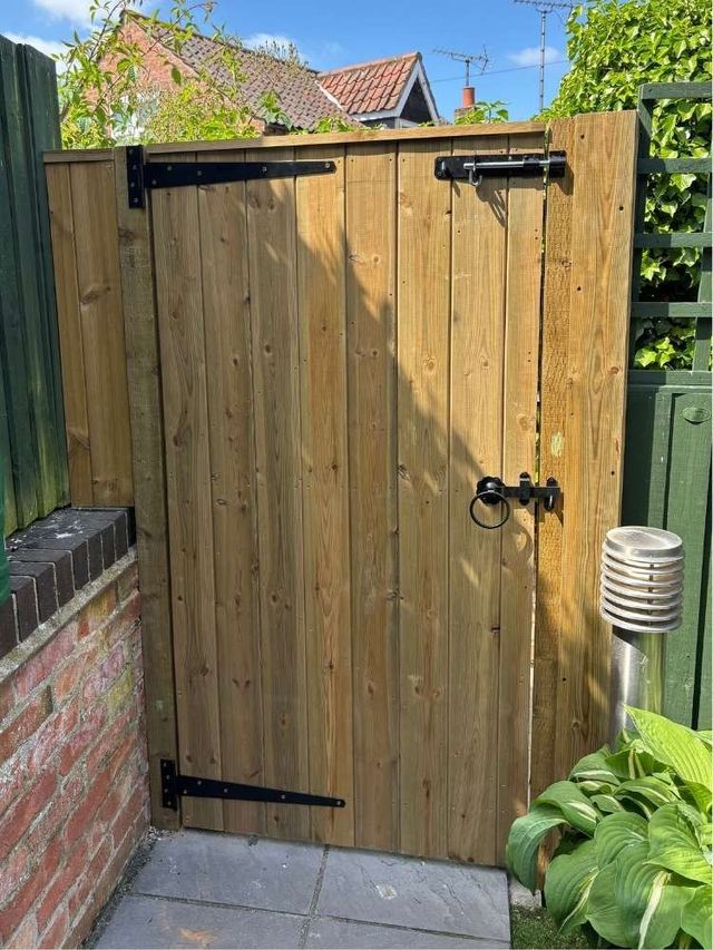 Heavy tongue and groove garden gate with long black strap hinges top and bottom, a slide bolt, lock and ring handle