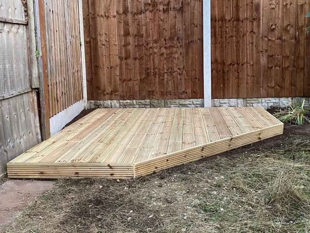 Small timber deck with a cut corner built into the angle of a garden boundary against closeboard fence panels