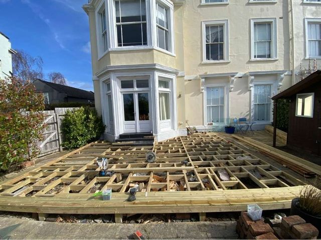 Timber decking sub frame of joists and bearers under construction across an old patio behind a rendered Victorian house