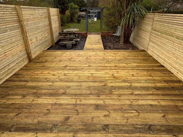 Wide timber deck in West Bridgford seen from the house, running between new slatted fence panels with a decked walkway leading to the lawn