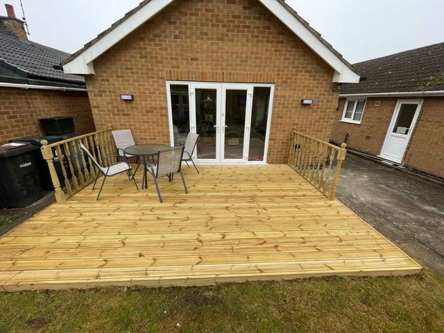 Timber deck outside bungalow patio doors with turned spindle balustrades on both sides and garden furniture in place