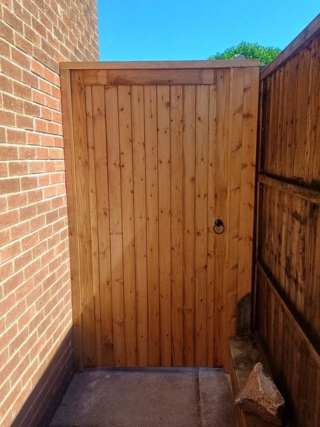 Framed tongue and groove pedestrian side gate with a capping rail across the top, between a brick wall and a closeboard fence