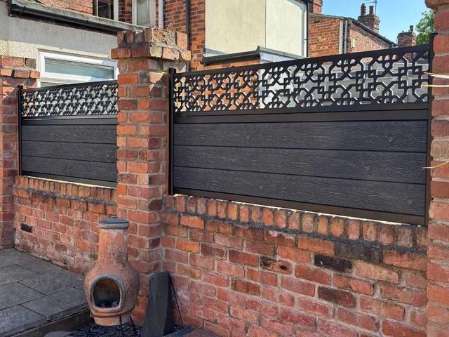 Anthracite grey composite fencing with cathedral screening mounted on an old red brick wall