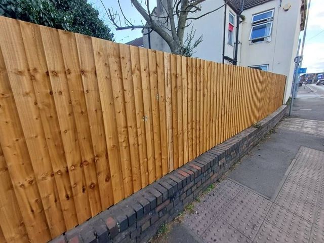 Closeboard timber fencing mounted on a low brick wall along a pavement