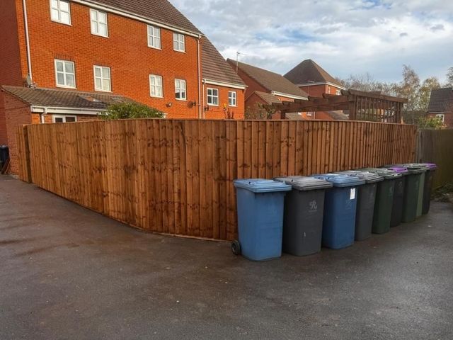 Closeboard timber fencing enclosing the rear of a property with wheelie bins along a service road