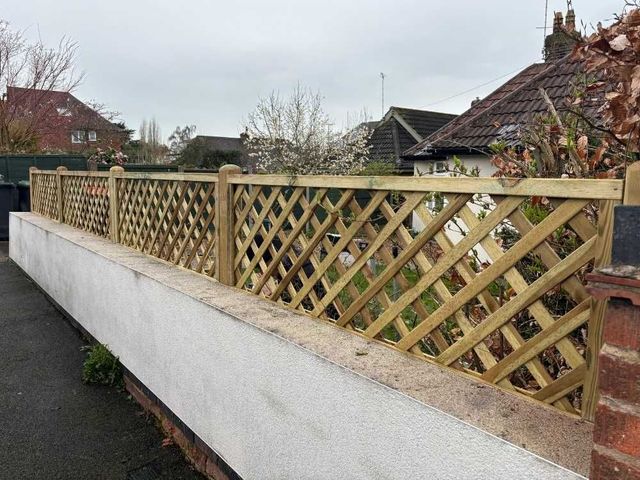 The same trellis topped wall seen from the pavement, stepping down along a rendered and capped roadside boundary