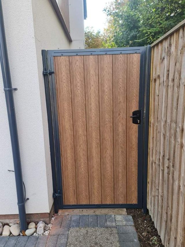 Walnut composite side gate in an anthracite grey metal frame between a house and fence