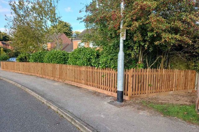 New picket fencing running along a pavement past a street lamp with a laurel hedge behind in Forest Town
