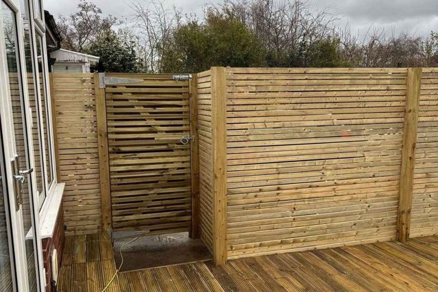 Horizontal slatted timber fencing and a matching slatted gate around decking in West Bridgford