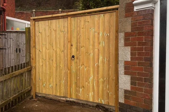 Tongue and groove timber double gates with a ring latch fitted between a brick pier and a house wall