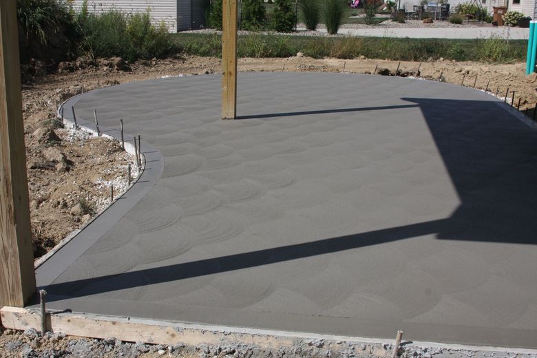 Freshly poured concrete patio foundation with wooden posts and a curved edge in a yard.