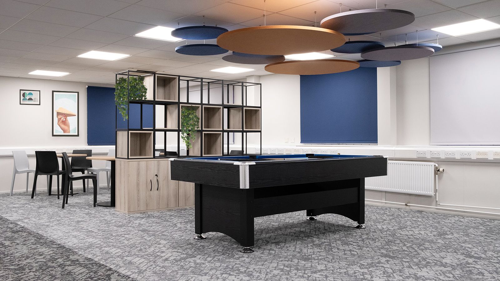 Pool table in the centre of the room underneath blue and orange acoustic hanging panels.