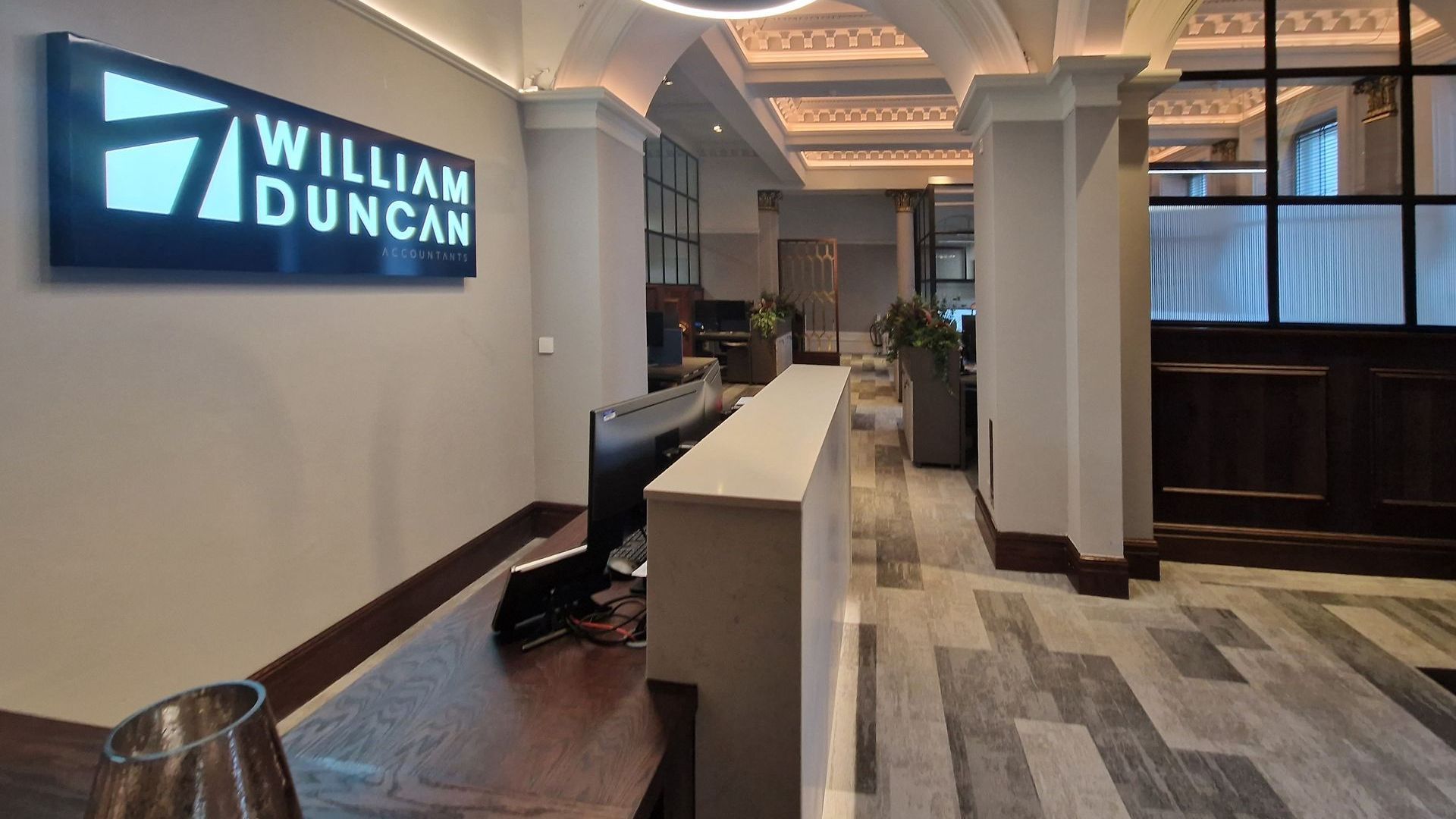 Reception at William Duncan office in Kilmarnock. Behind the front desk are monitors and a desk chair.
