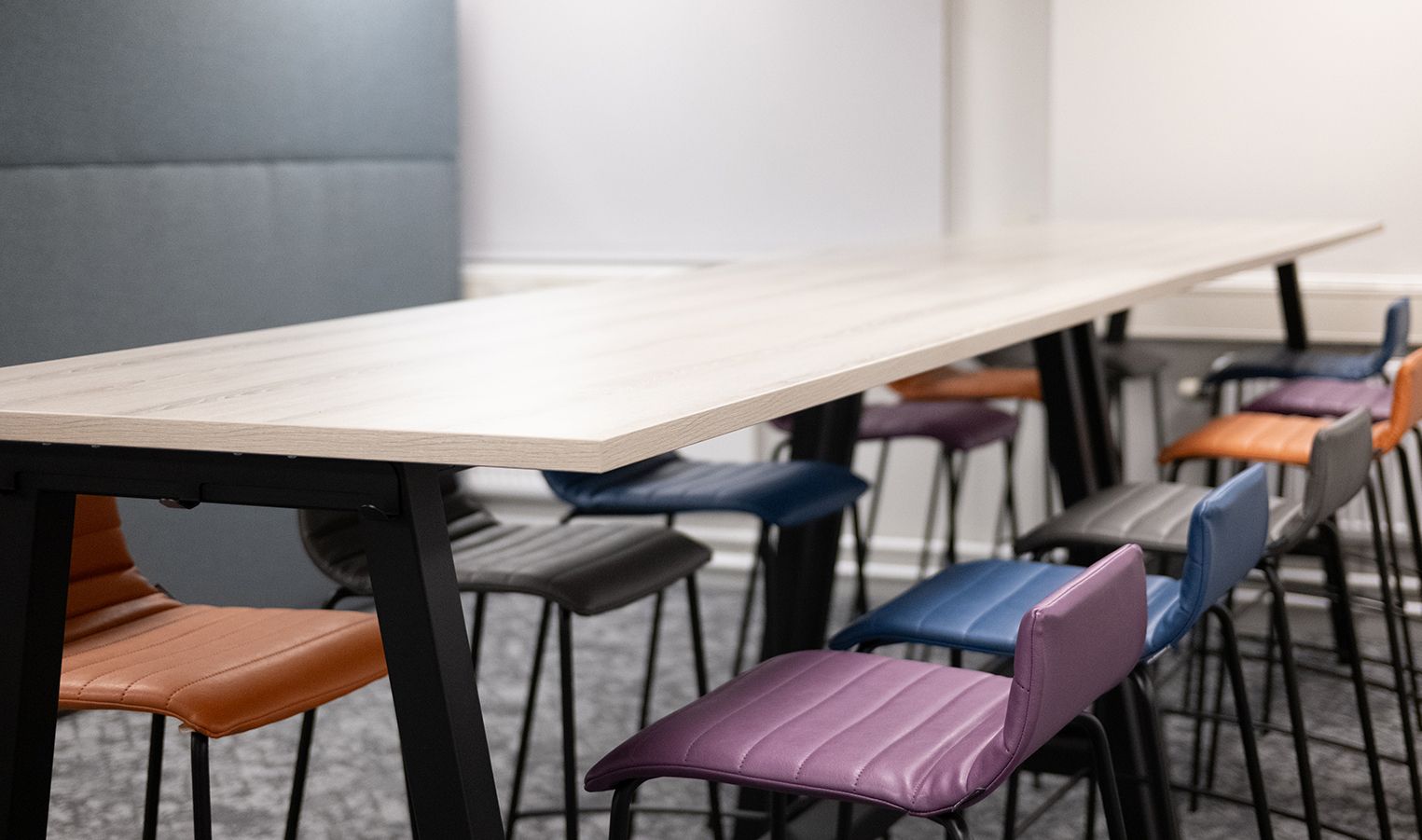 Close-up photos of multi-coloured stools at a high table. The stools are purple, blue, grey and orange.