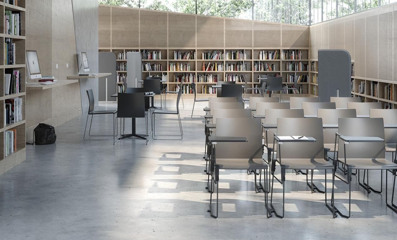 Modern library with rows of chairs, bookshelves, computers, and natural light streaming through large windows.