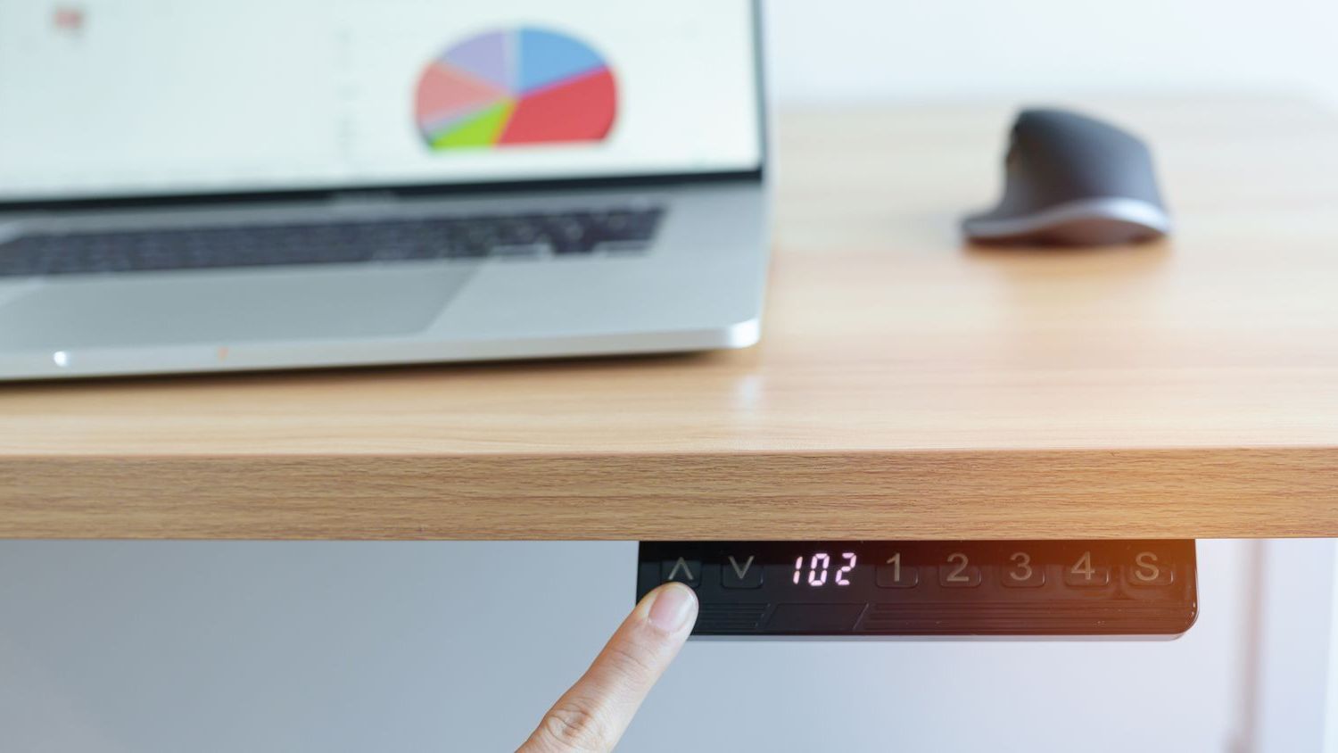 A finger pressing the adjustable buttons on a height-adjustable desk to raise and lower the desk.
