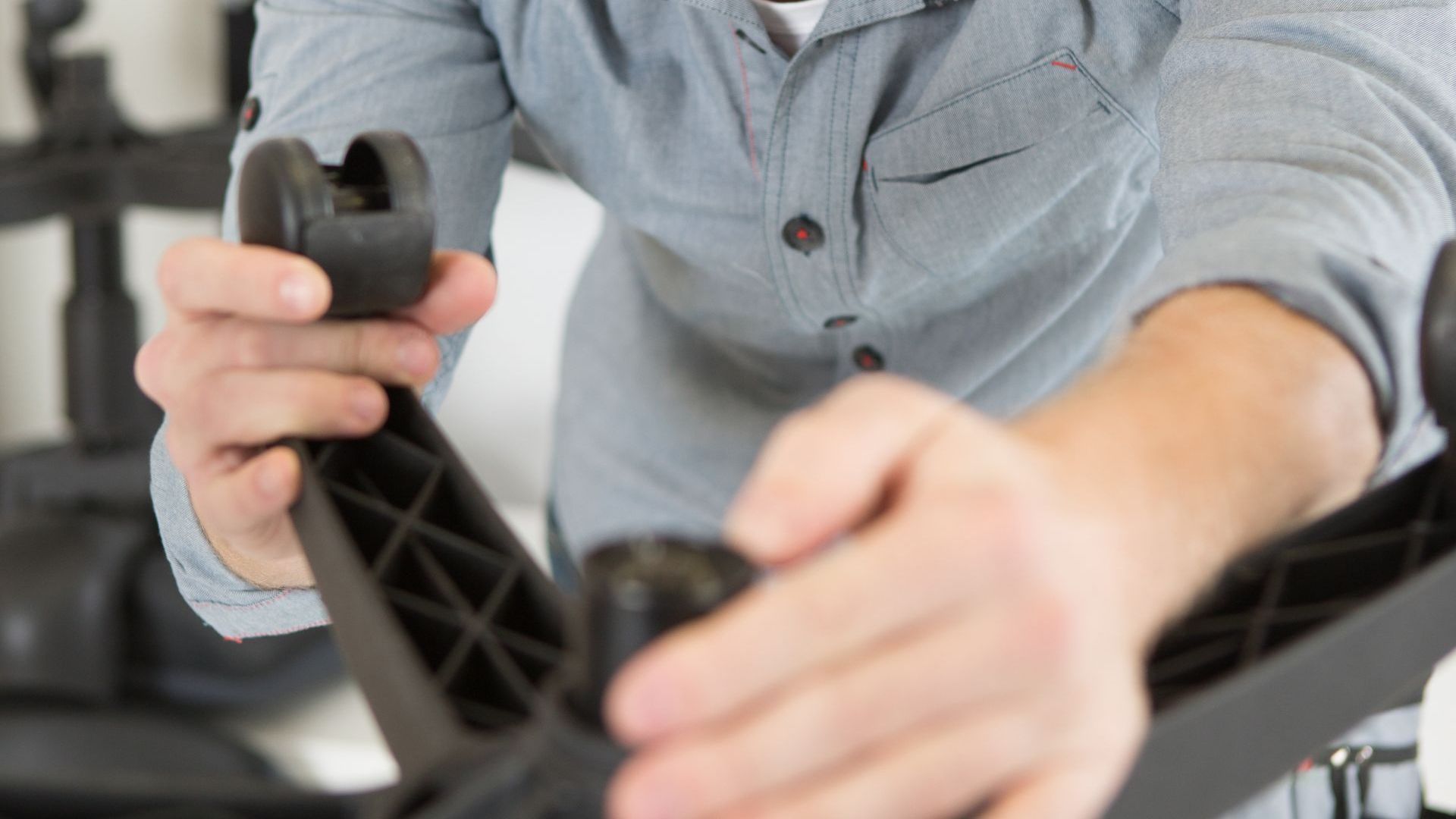 Person assembling a black office chair base, wearing a blue shirt.