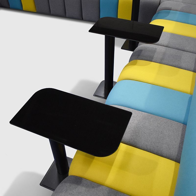 Black tables with rounded corners next to a colorful modular sofa in yellow, blue, and gray.