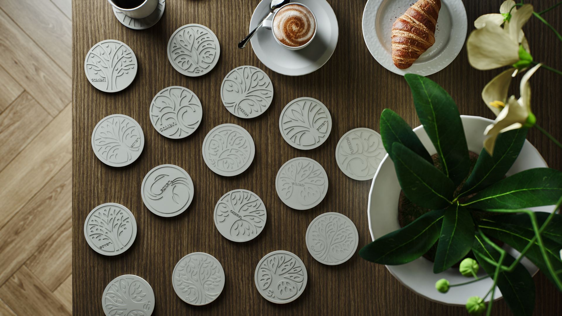 Wooden table with coasters, pastries, coffee cup, and floral arrangement.