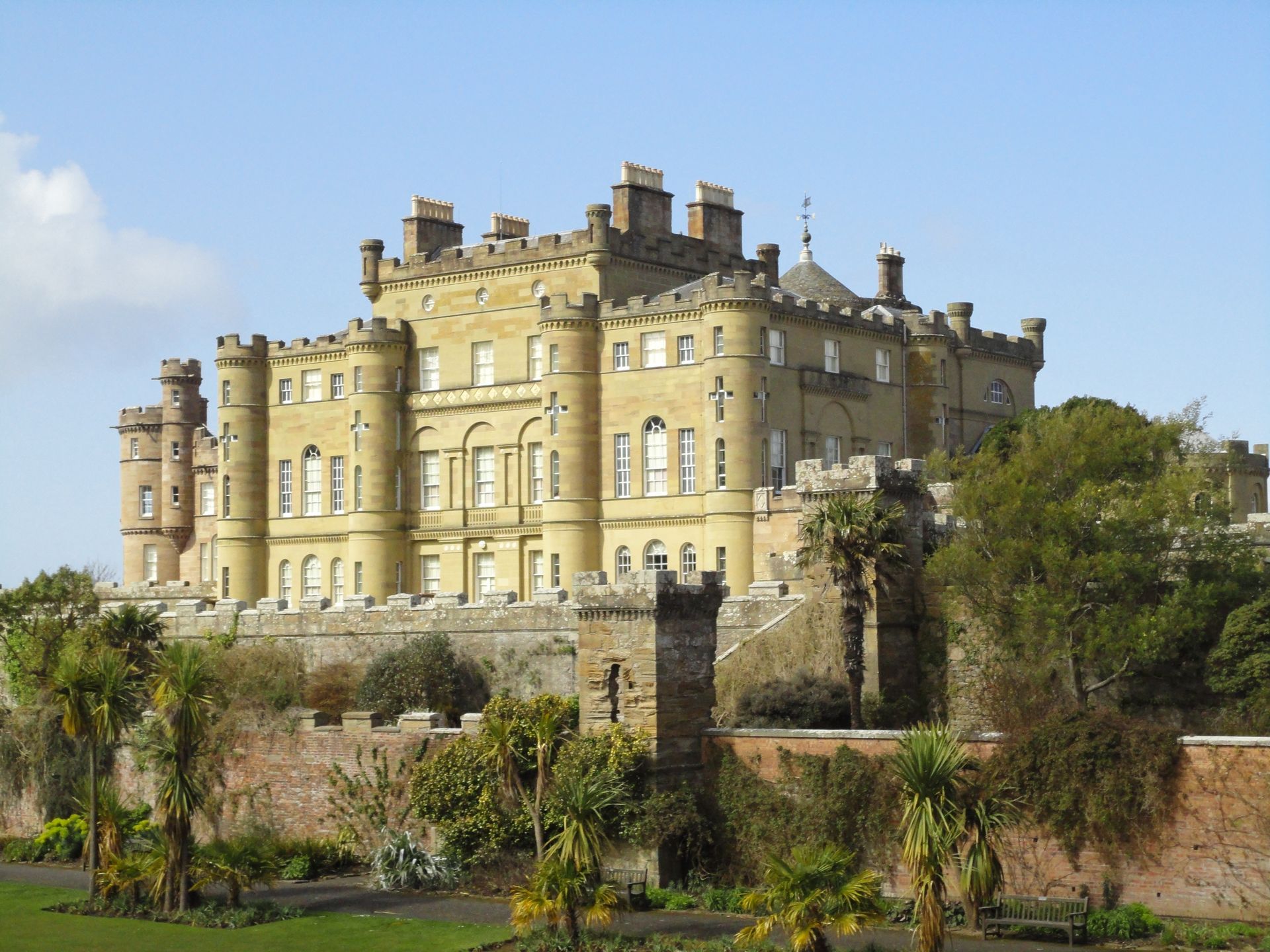 A grand stone castle on a raised foundation against a blue sky, with palm trees in front.