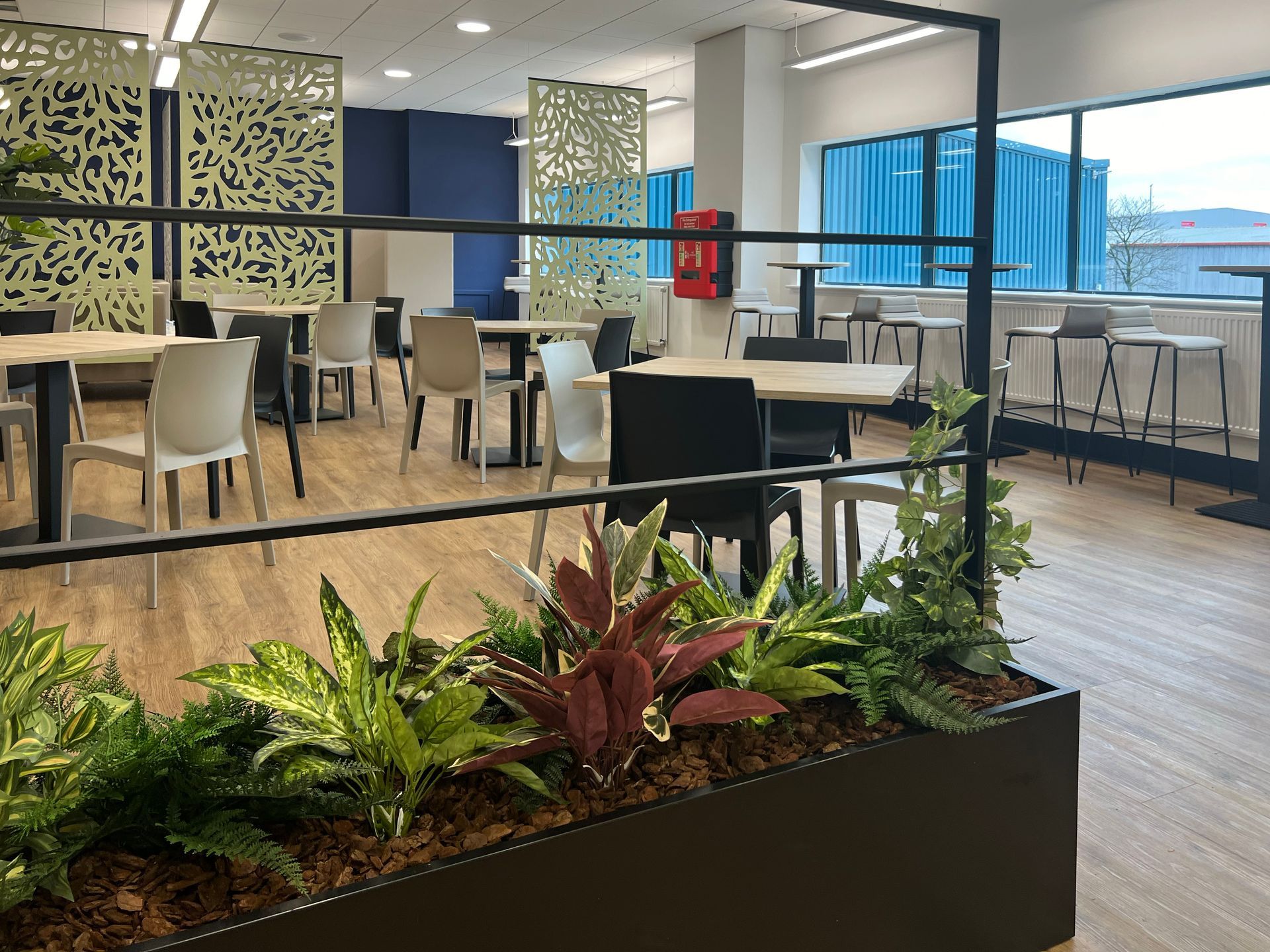 Café and collaborative meeting space with planters, bistro tables and chairs, and acoustic panels.