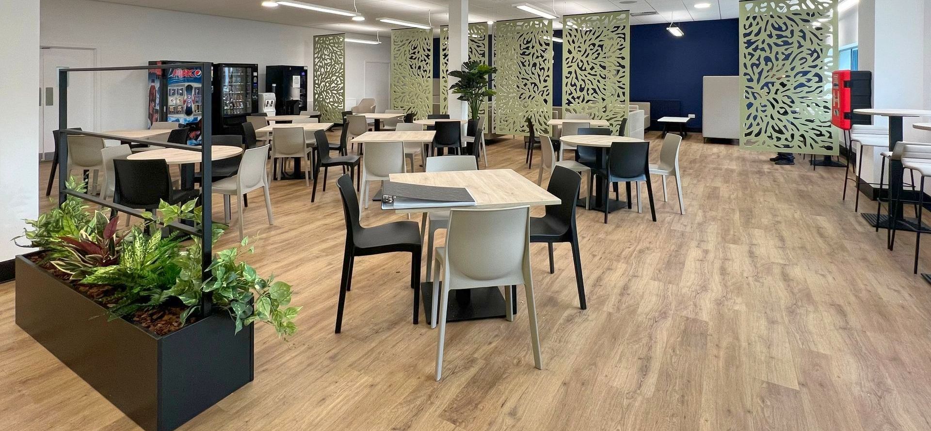 Autex acoustic ceiling-hung screens in a modern canteen space with bistro tables, café chairs, soft seating and planters,