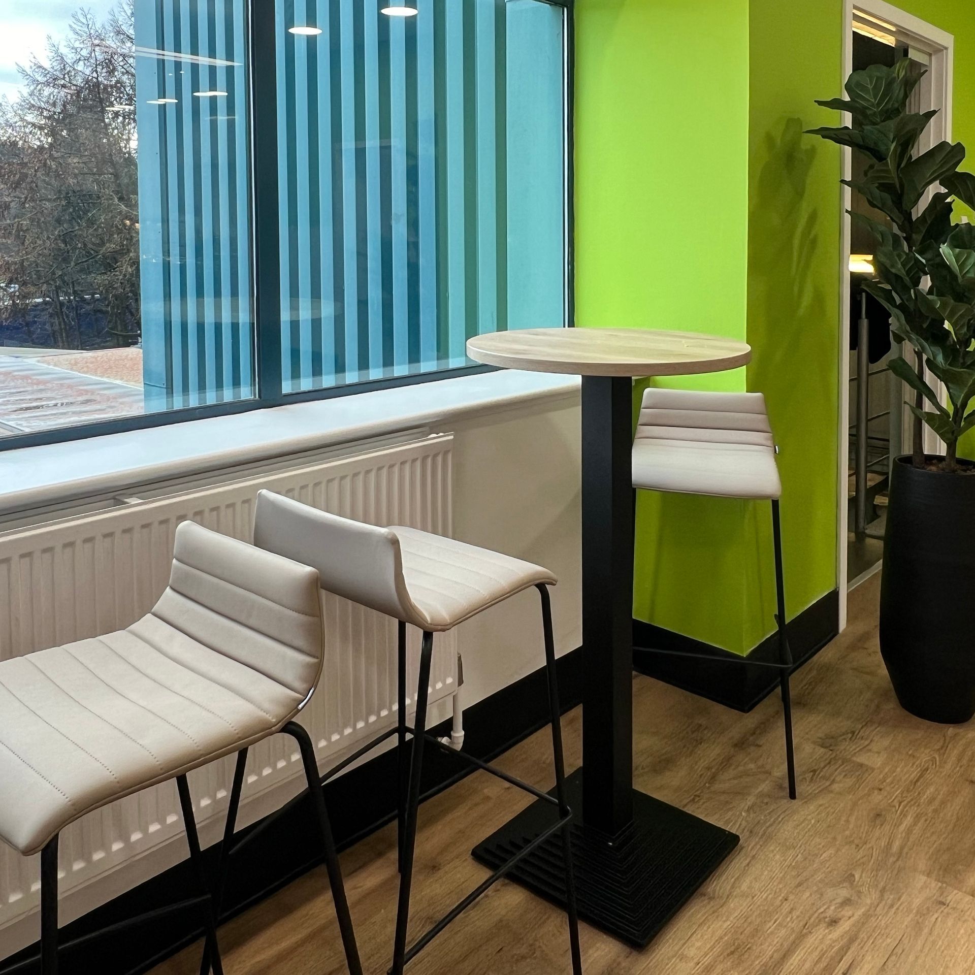 Poseur height bistro tables and upholstered high stools sit in front of a window.