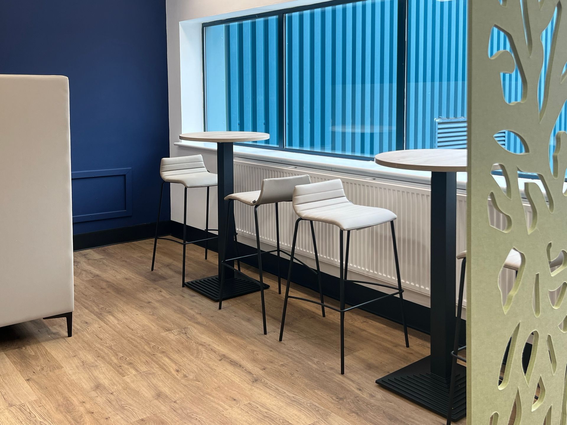 Poseur height bistro tables and upholstered high stools sit in front of a window.